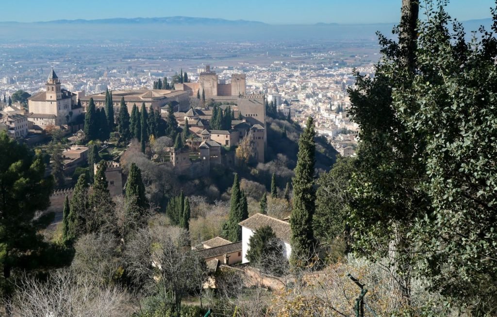 Stunning view of the Alhambra with Granada cityscape in Spain, surrounded by lush cypress trees.